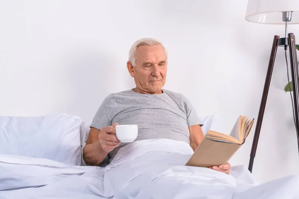 Retrato Homem Sênior Com Xícara Livro Leitura Café Cama Casa — Fotografia de Stock