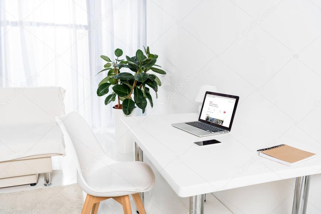 Home office with laptop with airbnb logo, smartphone and notebook on table