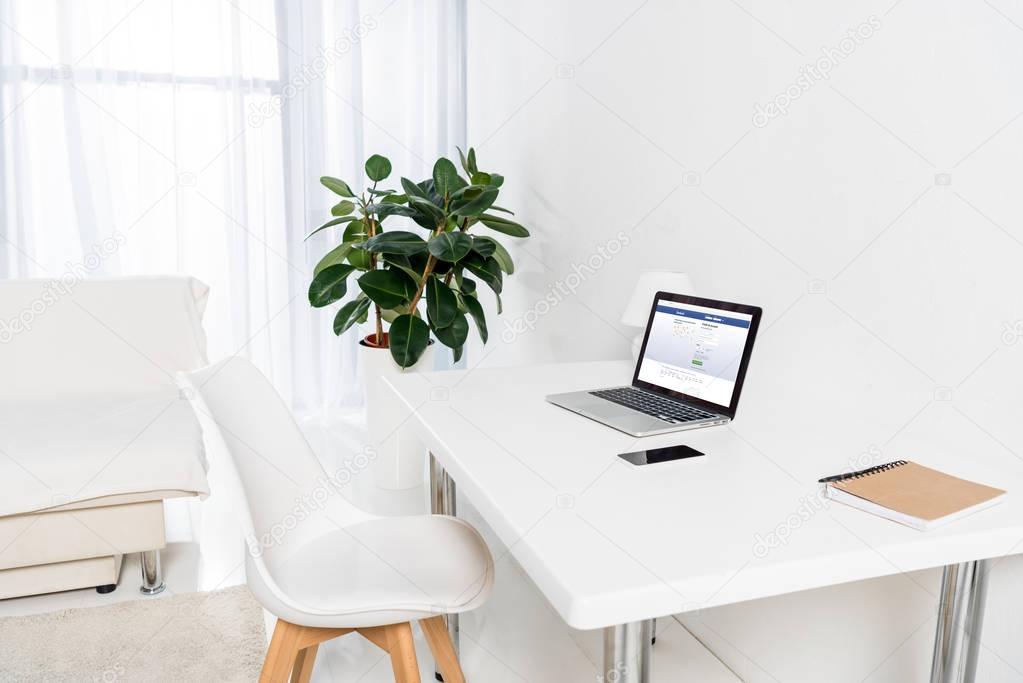 Home office with laptop with facebook logo, smartphone and notebook on table