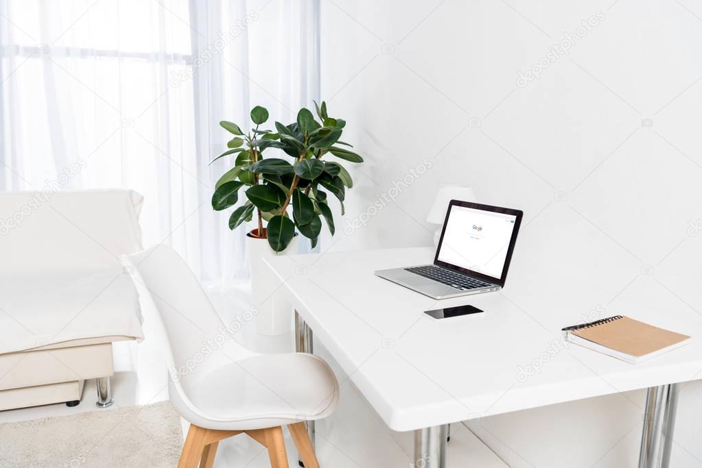 Laptop with google logo, smartphone and notebook on table in living room