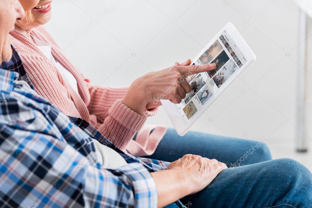 Cropped shot of smiling senior man and woman using digital tablet with pinterest logo on screen together