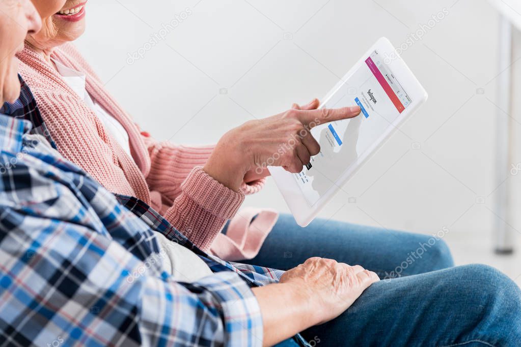 Cropped shot of smiling senior man and woman using digital tablet with instagram logo on screen together