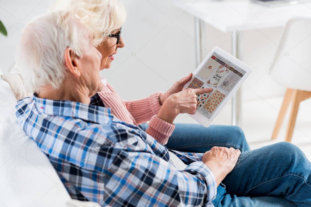 Side view of senior couple using digital tablet with pinterest logo together