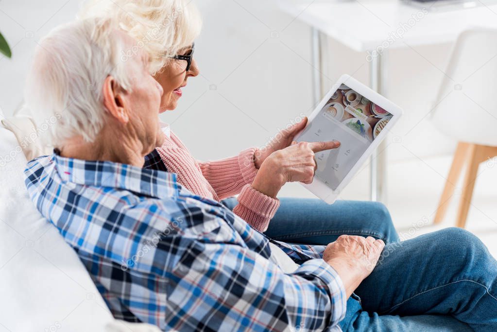 Side view of senior couple using digital tablet with foursquare logo together