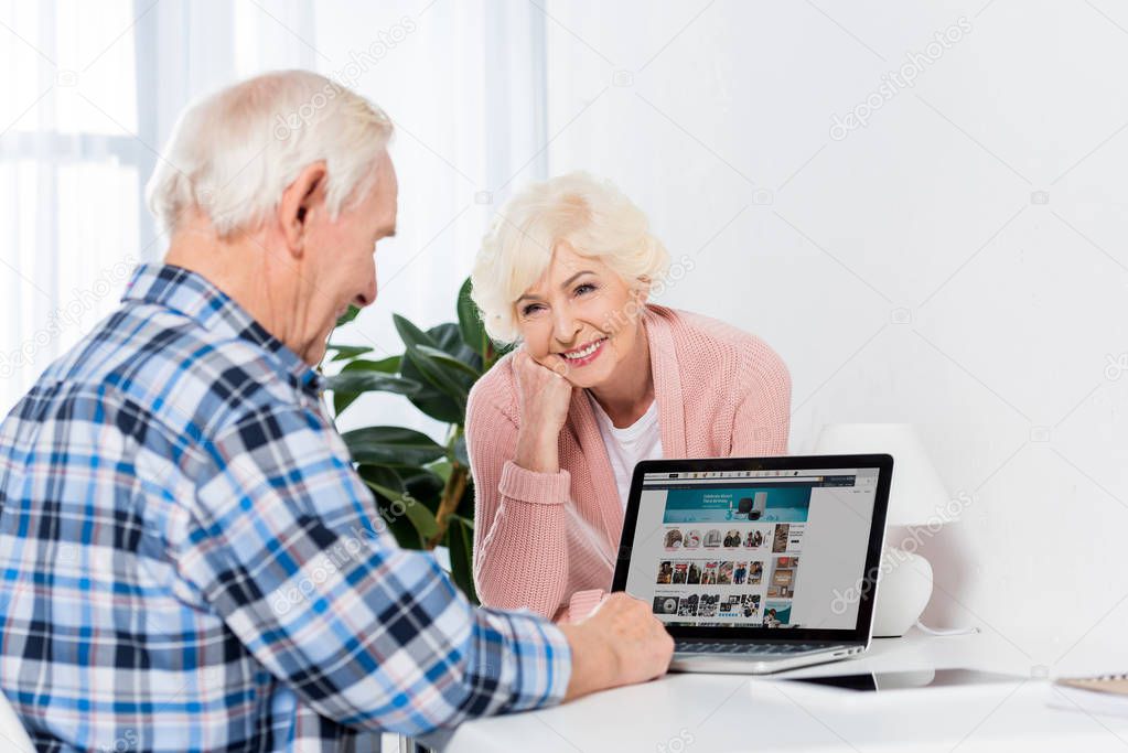Portrait of senior wife looking at husband using laptop at home