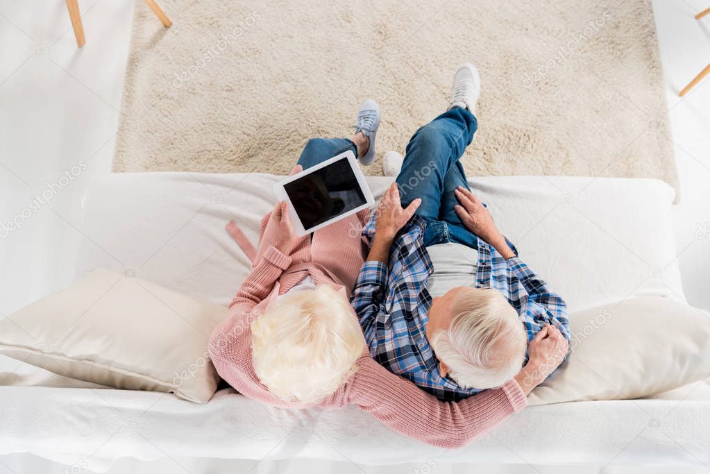 overhead view of senior couple with tablet resting on sofa at home