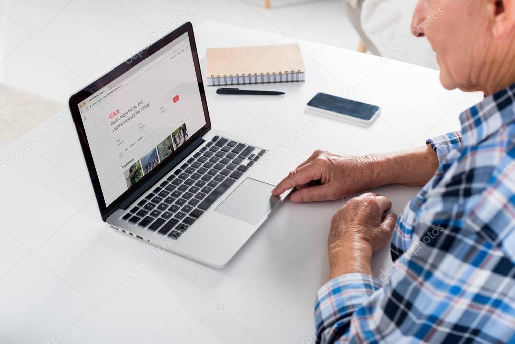 Partial view of senior man sitting at table and using laptop with airbnb logo