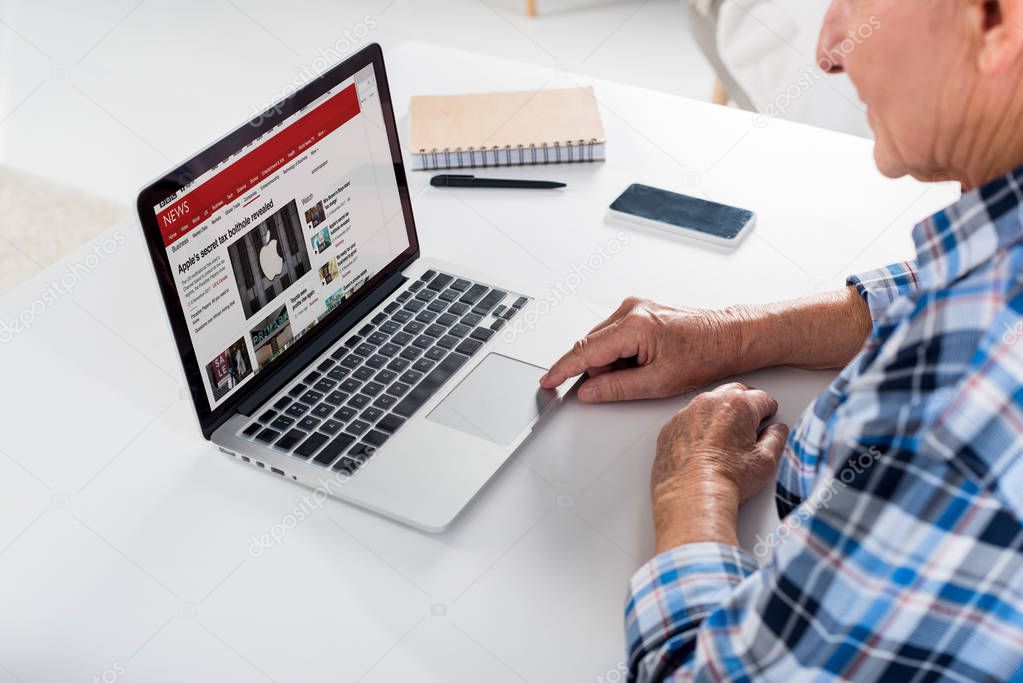 Partial view of senior man sitting at table and using laptop with bbc logo