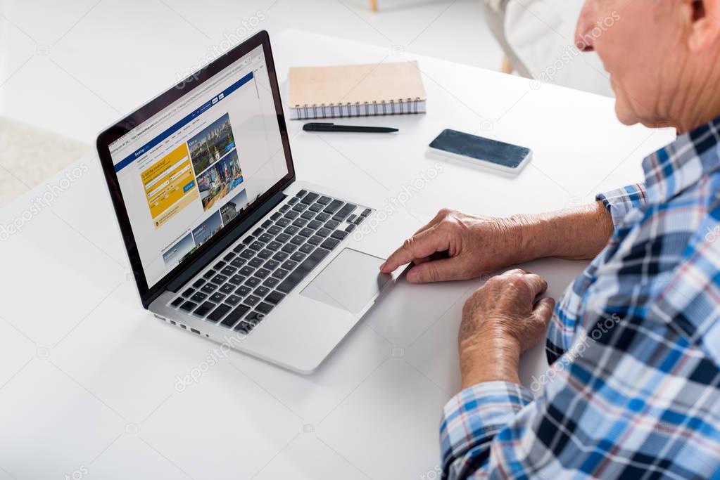Partial view of senior man sitting at table and using laptop with booking com logo
