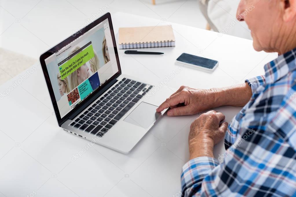 Partial view of senior man working on laptop with bbc logo at table with notebook at home