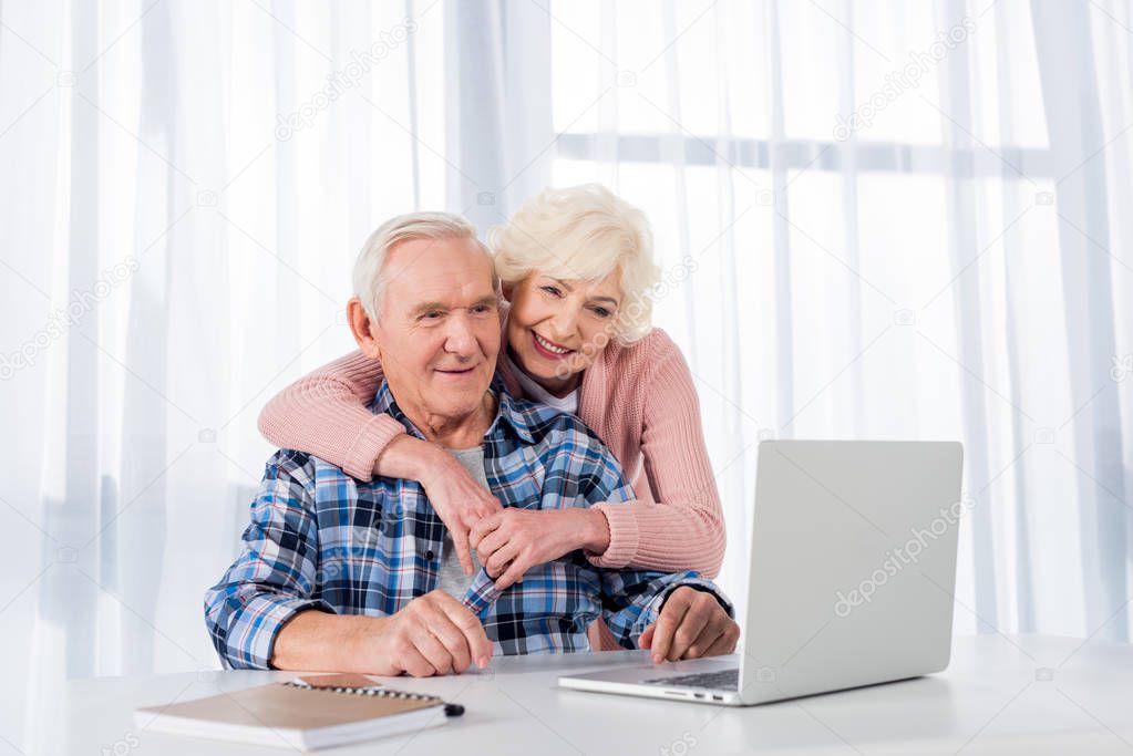 portrait of cheerful senior couple using laptop together at home