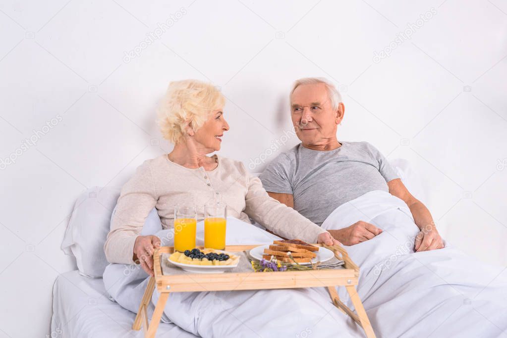 happy senior couple having breakfast in bed together at home