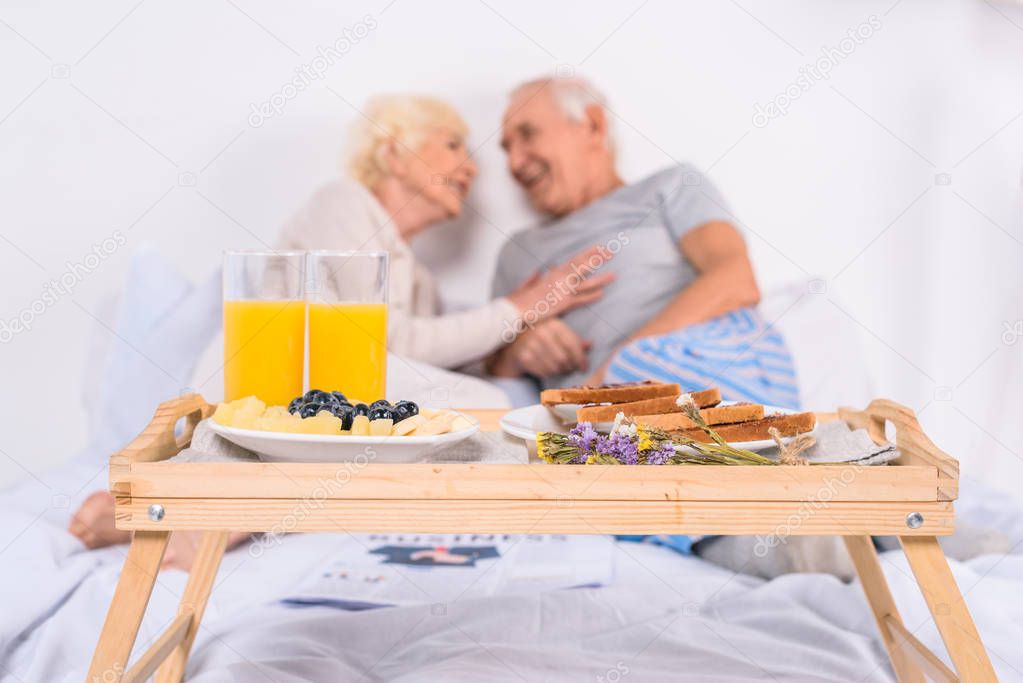 selective focus of breakfast and happy senior couple in bed at home