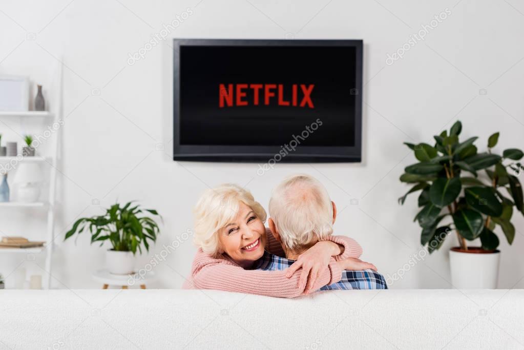 Senior couple embracing on couch in front of tv with netflix logo on screen