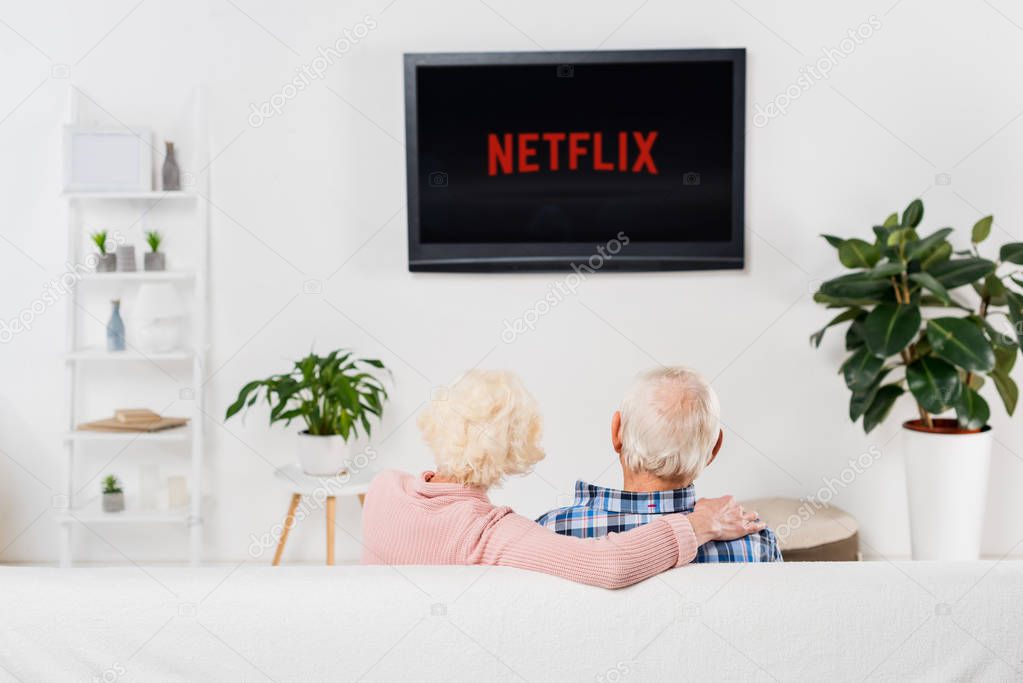 Back view of senior couple watching netflix on tv at home