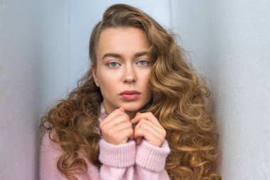 portrait of serious girl with long curly hair looking at camera and standing between walls clipart
