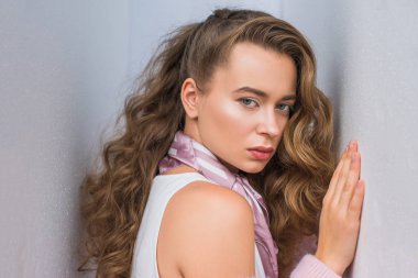 gri duvara yaslanmış ve moda çekimi için poz kıvırcık saçlı çekici kız