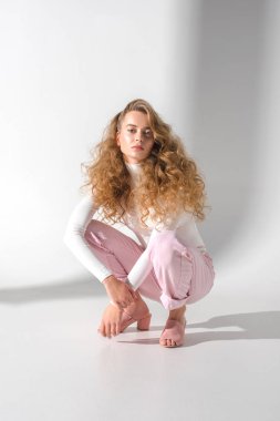 çömelme ve kameraya bakarak kıvırcık saçlı güzel kız