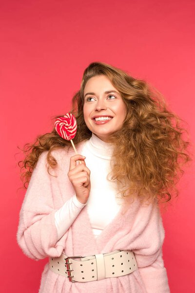 smiling girl holding heart shaped lollipop isolated on red