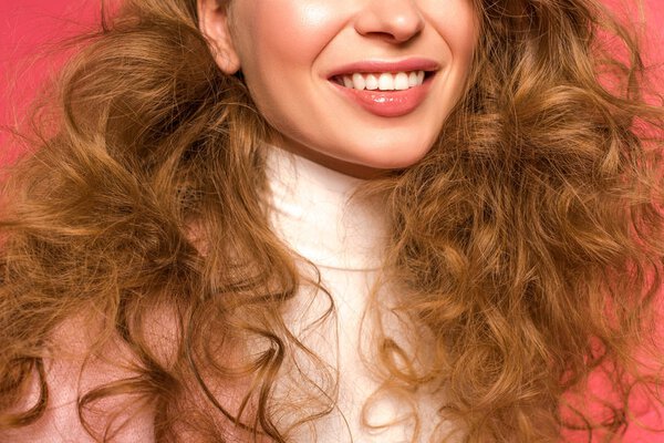 Обрезанное изображение улыбающейся девушки с вьющимися волосами на красном
