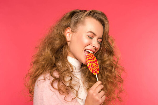 attractive girl biting round lollipop isolated on red