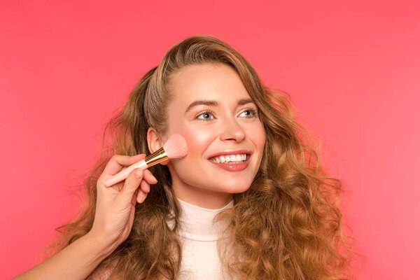 cropped image of woman doing makeup for smiling girl isolated on red