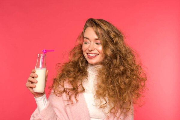 smiling girl looking at bottle with milkshake and plastic straw isolated on red