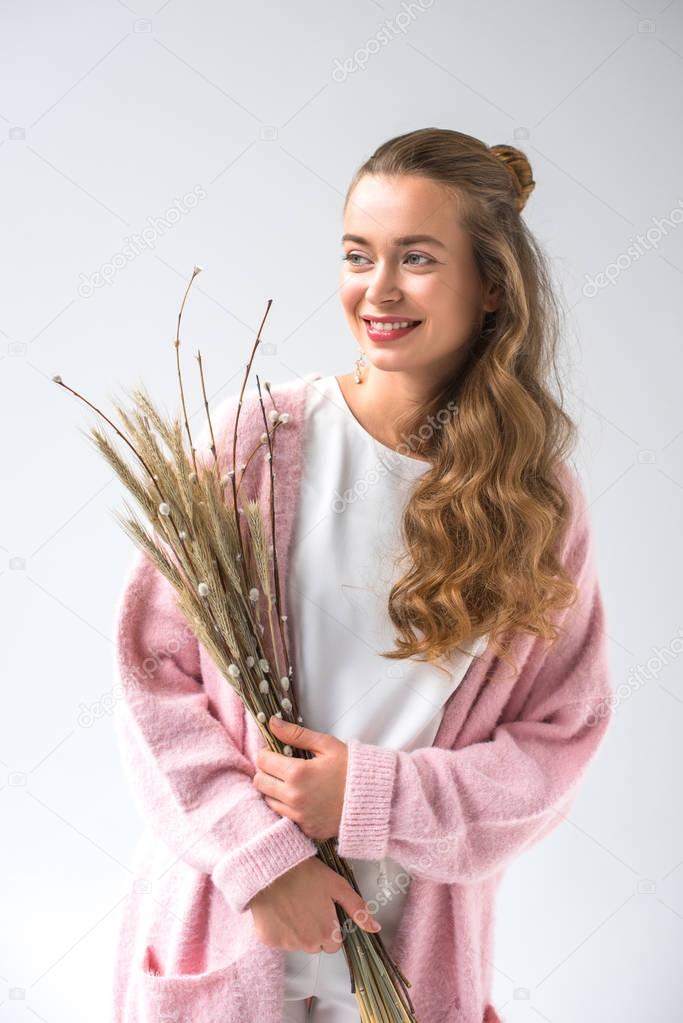 smiling woman holding bunch of willow tree branches and spikelets isolated on white