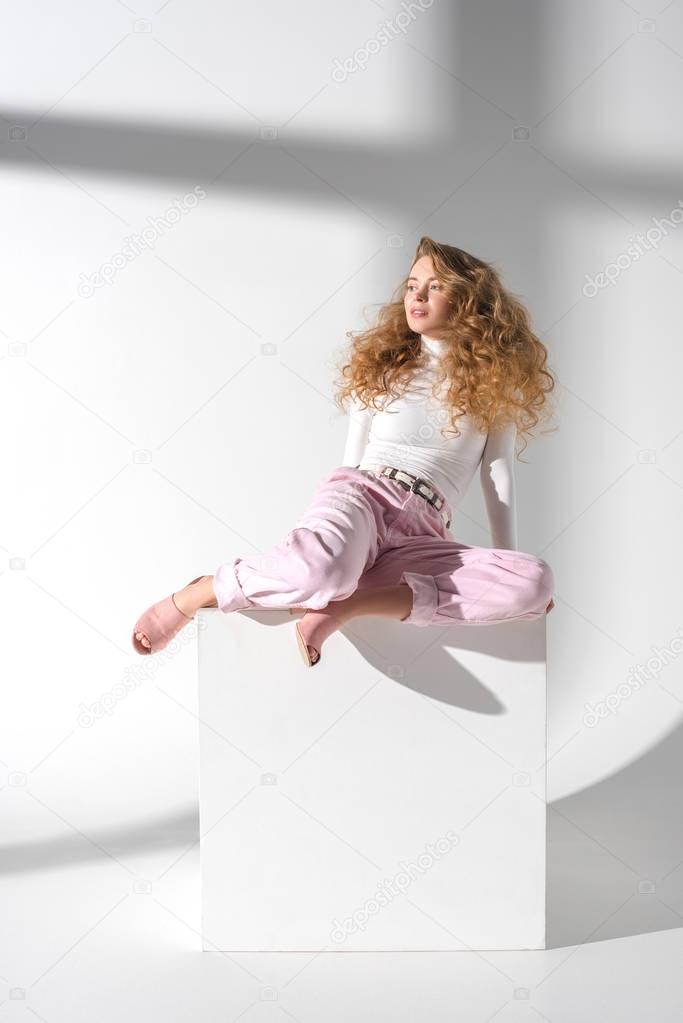 beautiful girl sitting on white cube and looking away