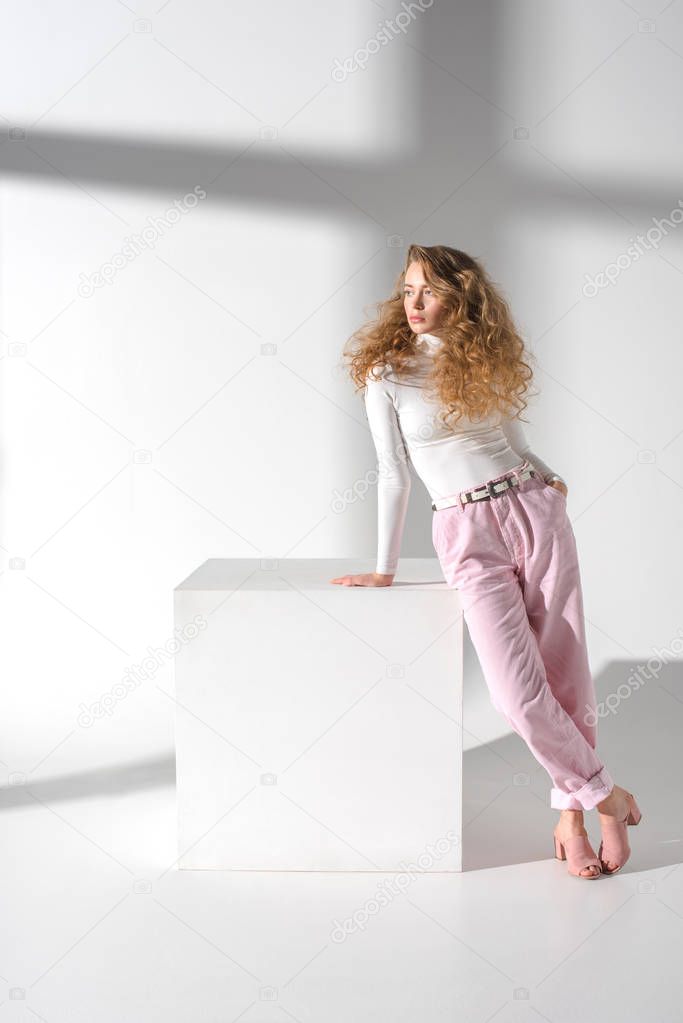 Stylish confident woman standing and leaning on white cube