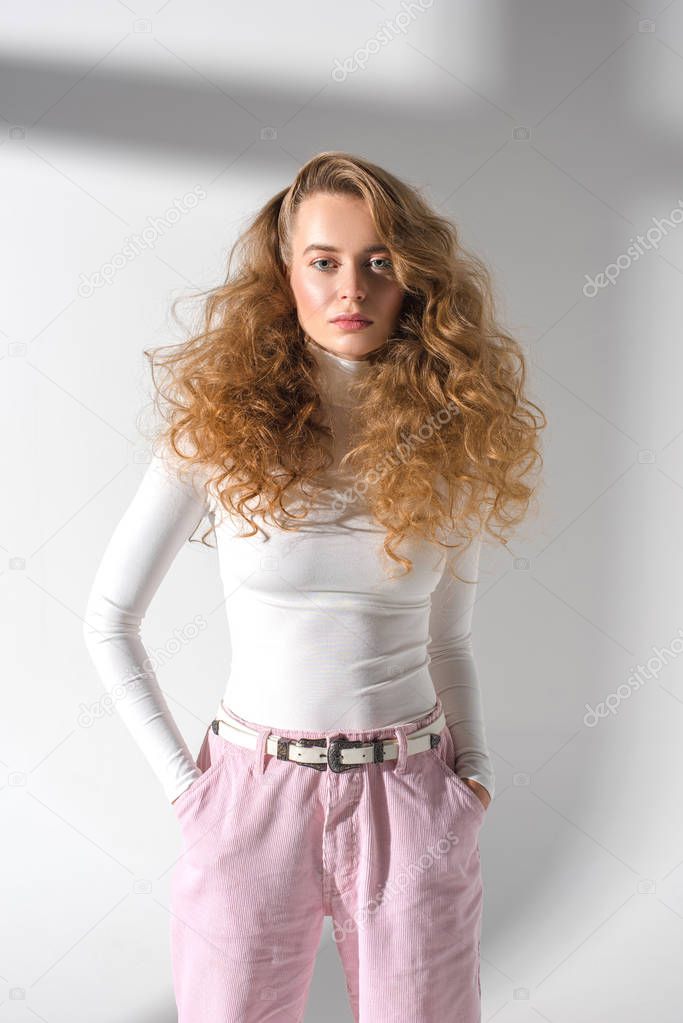 attractive stylish woman with curly hair standing with hands in pockets 