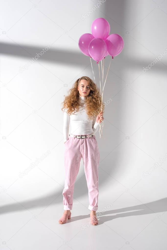 serious girl in stylish outfit standing with pink balloons with helium
