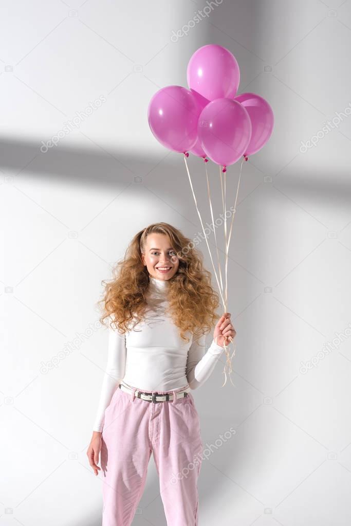 happy woman standing with balloons with helium and looking at camera