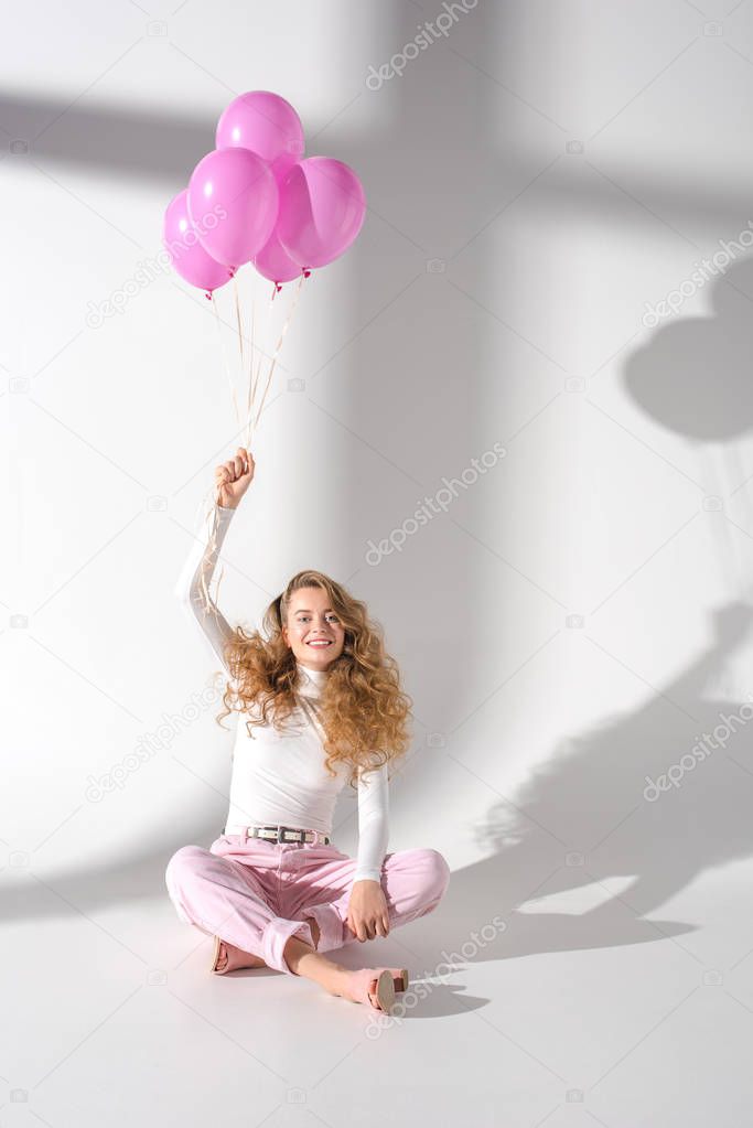 happy beautiful girl with hand up sitting and holding bundle of balloons