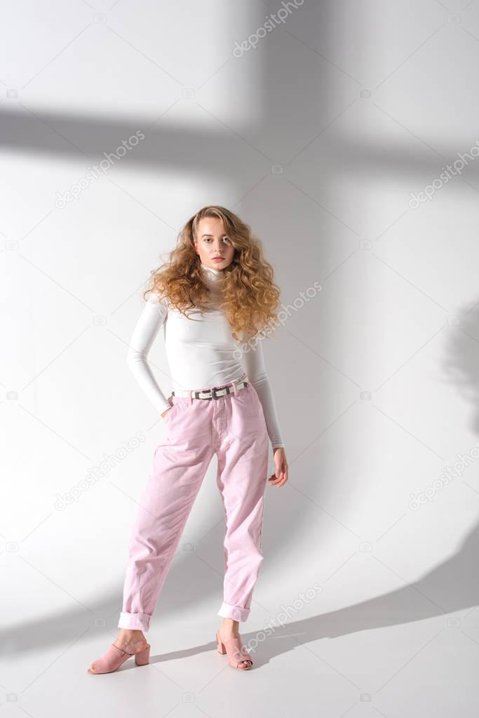 fashionable girl with curly hair standing and looking at camera