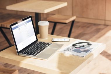 laptop, smartphone with facebook messenger and business newspaper on table in coffee shop clipart