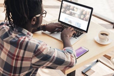 Afrika kökenli Amerikalı adam dizüstü depositphotos Web sitesi ve smartphone ile instagram cihaz ile kullanma