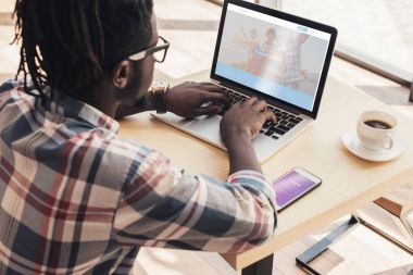 Afrikalı-Amerikalı adam dizüstü couchsurfing Web sitesi ve smartphone ile instagram cihaz ile kullanma