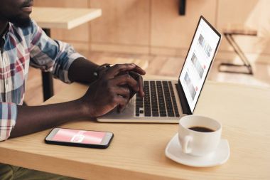 kafede youtube Web sitesi ile smartphone ve dizüstü bilgisayar kullanan Afrikalı-Amerikalı adam görünümünü kırpılmış