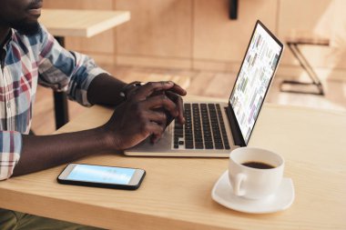 Afrika kökenli Amerikalı adam smartphone ile skype ile pinterest Web sitesi kafede dizüstü bilgisayar kullanıyorsanız ve görünümünü kırpılmış