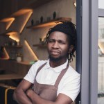 African american cafe owner in apron standing with crossed arms at entrance