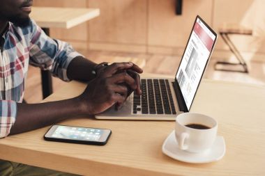 bbc haber sitesi ve kafede smartphone ile dizüstü bilgisayar kullanan Afrikalı-Amerikalı adam görünümünü kırpılmış