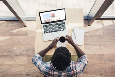 Afrika kökenli Amerikalı adam kahve içme ve dizüstü bilgisayar ile ebay Web sitesi kullanarak havai görünümü