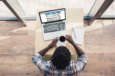 Afrika kökenli Amerikalı adam kahve içme ve dizüstü bilgisayar ile amazon Web kullanarak havai görünümü