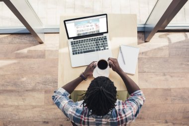 Afrika kökenli Amerikalı adam kahve içme ve airbnb Web sitesi ile dizüstü bilgisayar kullanarak havai görünümü