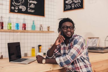 smartphone üzerinde konuşmak ve cafe bar counter laptop kullanarak gülümseyen Afrikalı-Amerikalı adam