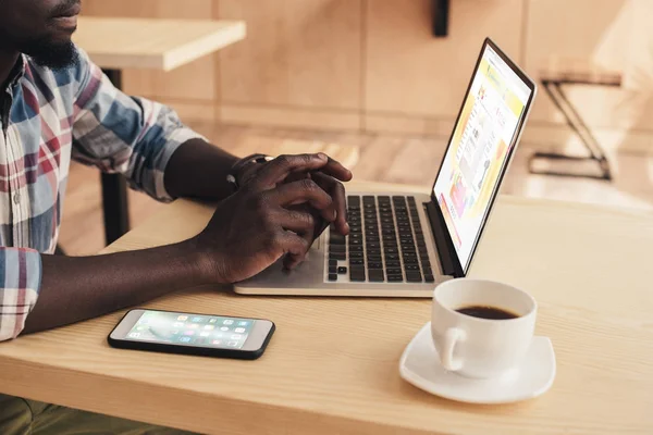 커피숍에서 Aliexpress 웹사이트와 스마트폰 노트북을 아프리카계 미국인 남자의 — 스톡 사진