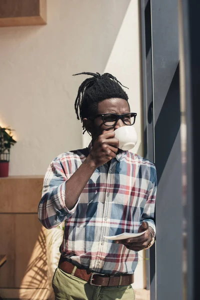 Afryki Amerykański Człowiek Okularach Picie Kawy Stojąc Przy Oknie — Darmowe zdjęcie stockowe