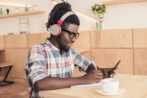 african american man listening music and using smartphone in coffee shop