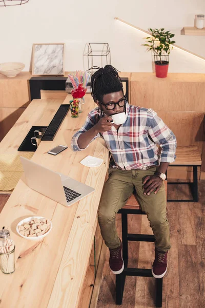 非洲裔美国人喝咖啡和使用手提电脑在酒吧柜台在咖啡馆 — 免费的图库照片